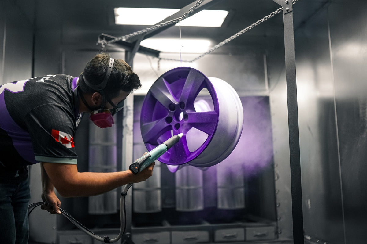 Applicateur peignant une jante en poudre violette au pistolet